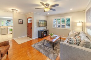 A living room with hardwood flooring, a ceiling fan, a television, a coffee table, and a sofa with patterned cushions.