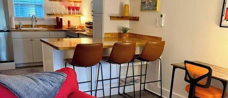 A compact living space with a kitchenette, a dining area with bar stools, a red sofa, and a small table with a chair.