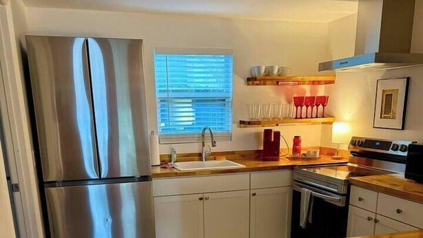 Eine Küche mit Edelstahlkühlschrank, Holz-Arbeitsplatten und weißen Schränken.