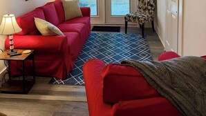 Ein Wohnzimmer mit einem roten Sofa, einem gemusterten Teppich, einem Sessel und einem an der Wand befestigten Fernseher.