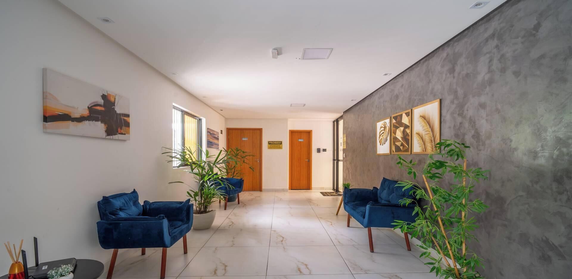 A hallway with two blue sofas, potted plants, and artwork on the walls.