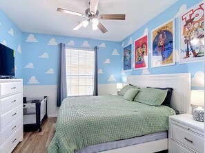 Ein Schlafzimmer mit Bett, Nachttisch, Schminktisch und Wanddekorationen sowie einem Deckenventilator.