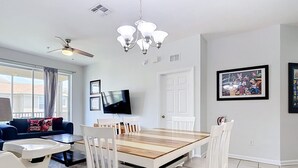 Un comedor con una mesa de madera y sillas blancas, un ventilador de techo y una lámpara de araña.