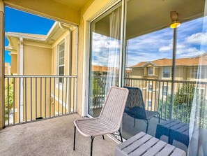 Ein Balkon mit Korbmöbeln, einem Tisch, großen Fenstern und Blick auf die Nachbarhäuser.