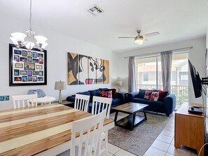 Ein Wohnzimmer mit Esstisch, Stühlen, einer Couch, einem Deckenventilator und einem großen Fenster mit Vorhängen.