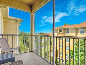 A balcony with a chair and a table, overlooking a residential area with houses and greenery. - Themed 2BR Condo Near Disney, Free Water Park (Kissimmee)