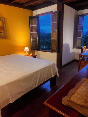 Una habitación con cama, una mesa y una ventana con contraventanas abiertas.