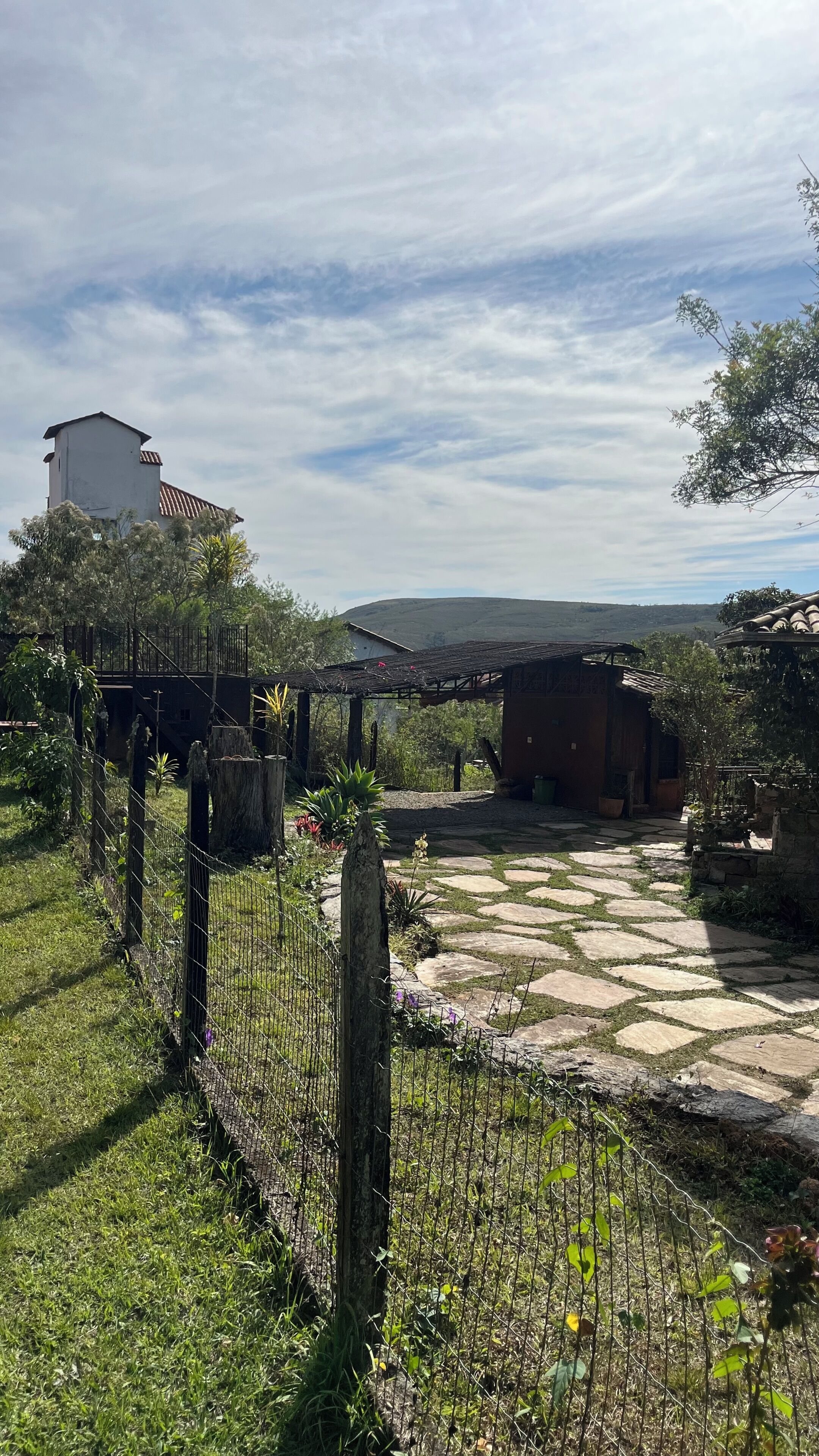 Un espacio exterior rústico con un sendero de piedra, construcciones de madera y un jardín cercado.