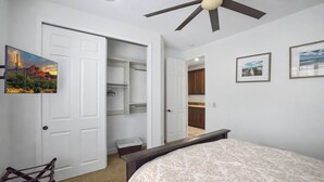 Quarto com cama, ventilador de teto, armário aberto, escrivaninha e uma cadeira.