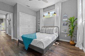 Quarto com cama, ventilador de teto, janela com cortinas e um vaso de planta.