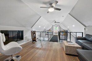 Ein geräumiges Dachzimmer mit hoher Decke, Deckenventilator und einer Treppe zu einer oberen Ebene.