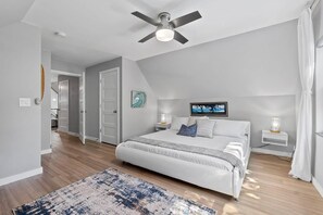 Ein Schlafzimmer mit einem Bett, Nachttischlampen, einem Deckenventilator und Blick auf einen Flur.
