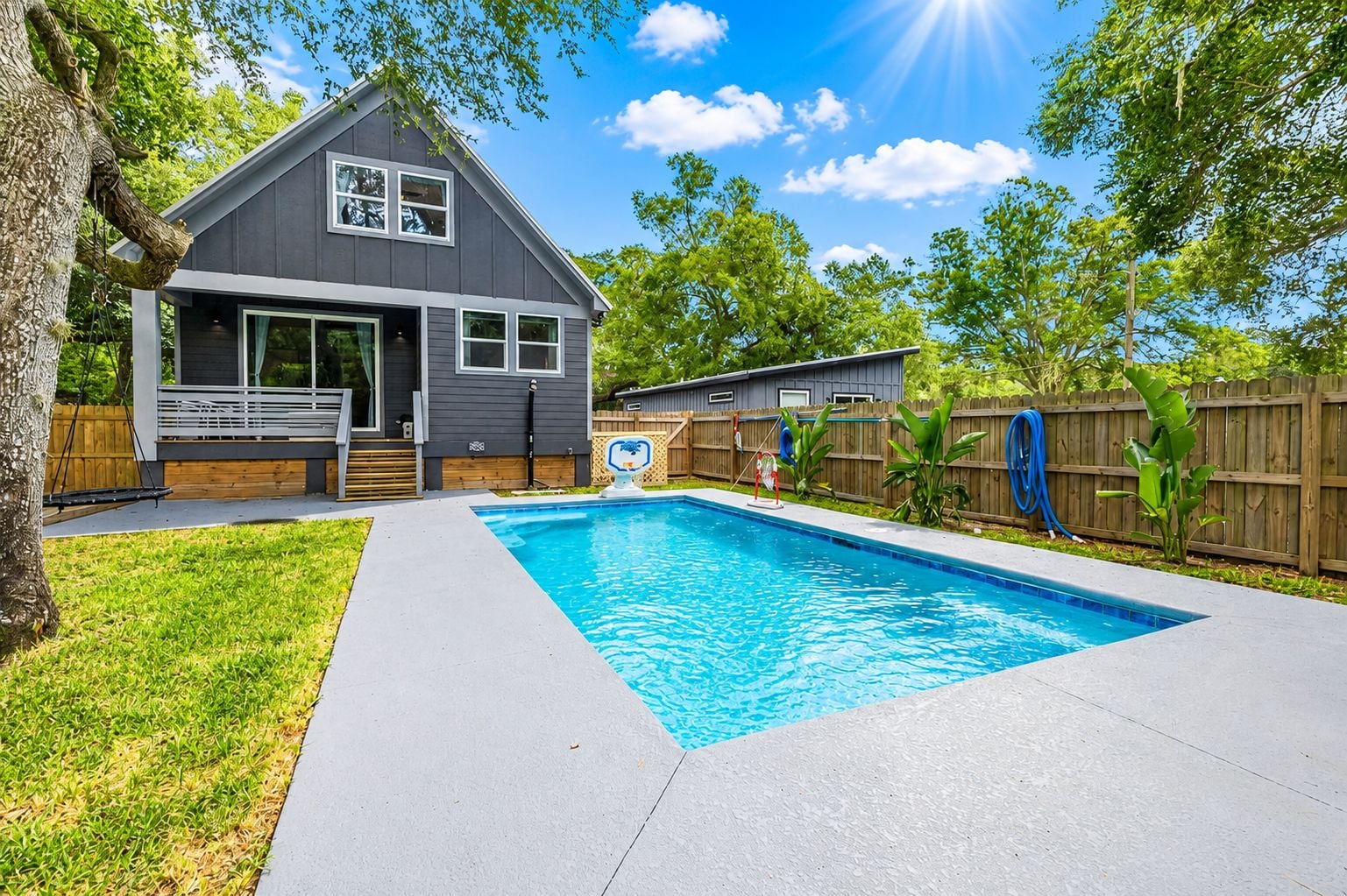 A residential backyard with a swimming pool, a house, and a wooden fence.