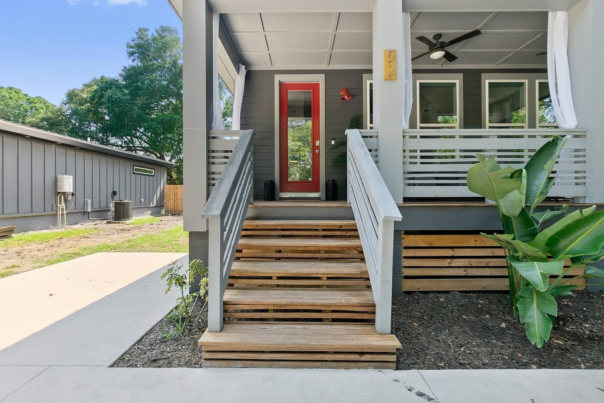 A building with a red door, wooden steps, a white railing, and a large plant.