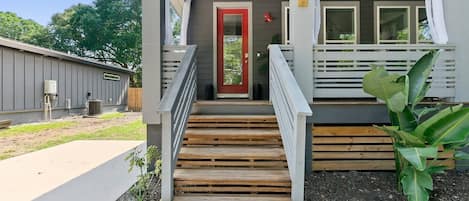 A building with a red door, wooden steps, a white railing, and a large plant.