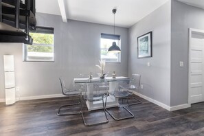 Uma área de jantar moderna com mesa de vidro, cadeiras transparentes e iluminação pendente.