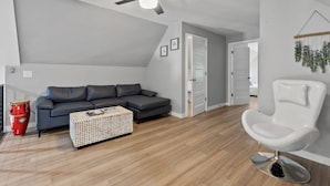 A modern living room with a sectional sofa, a white armchair, a ceiling fan, and a wooden floor. - St. Augustine with Private Pool Near Downtown (St. Augustine)