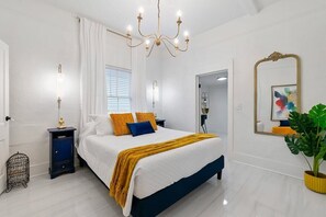 Ein Schlafzimmer mit einem Bett, Nachttischlampen, einer Chandelier, einem Spiegel und einer Topfpflanze.