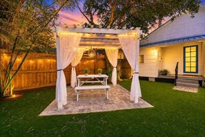 A covered outdoor seating area with a table and benches, surrounded by a wooden fence and a house with a window. - St. Augustine | Hot Tub | Parking | Walk Downtown (St. Augustine)