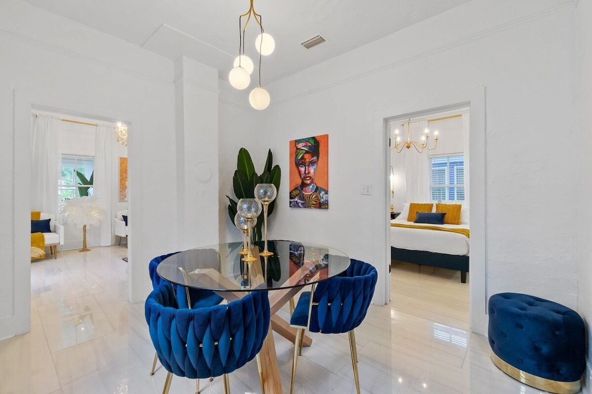 A modern dining area with a glass table, blue upholstered chairs, and a chandelier.