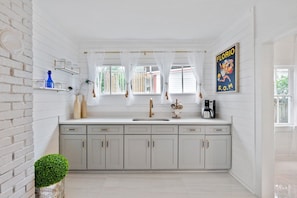 A kitchen with white cabinets, a sink, a coffee maker, and a window with sheer curtains. - St. Augustine | Hot Tub | Parking | Walk Downtown (St. Augustine)