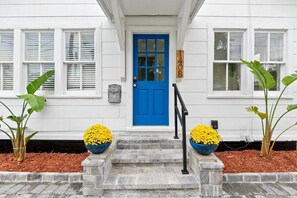 A white building with a blue door, numbered 140B, and a mailbox. There are steps leading to the door, and two potted plants with yellow flowers on either side. - St. Augustine | Hot Tub | Parking | Walk Downtown (St. Augustine)