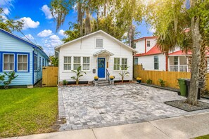 Ein Wohnhaus mit Veranda, einer blauen Tür und einer gepflasterten Auffahrt.