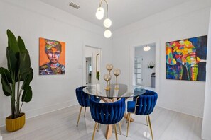 Ein stilvoller Essbereich mit einem Glastisch, blauen Samtstühlen und zwei Bildern an den Wänden.