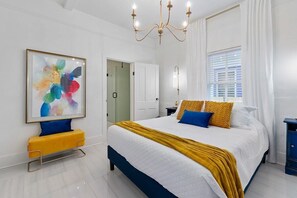 A bedroom with a large bed, a bedside table, a chair, a painting, and a chandelier. - St. Augustine | Hot Tub | Parking | Walk Downtown (St. Augustine)