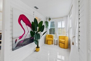 Une pièce aux murs blancs, ornée d’un grand tableau représentant un flamant rose, d’une plante en pot et de deux chaises jaunes.