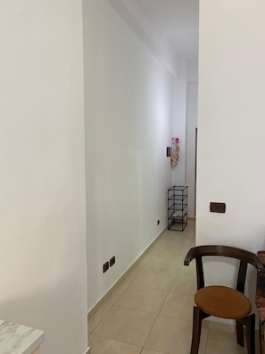 Ein Flur mit einem Stuhl, einem kleinen Tisch, einem Metallgestell und einem an der Wand montierten Thermostat.