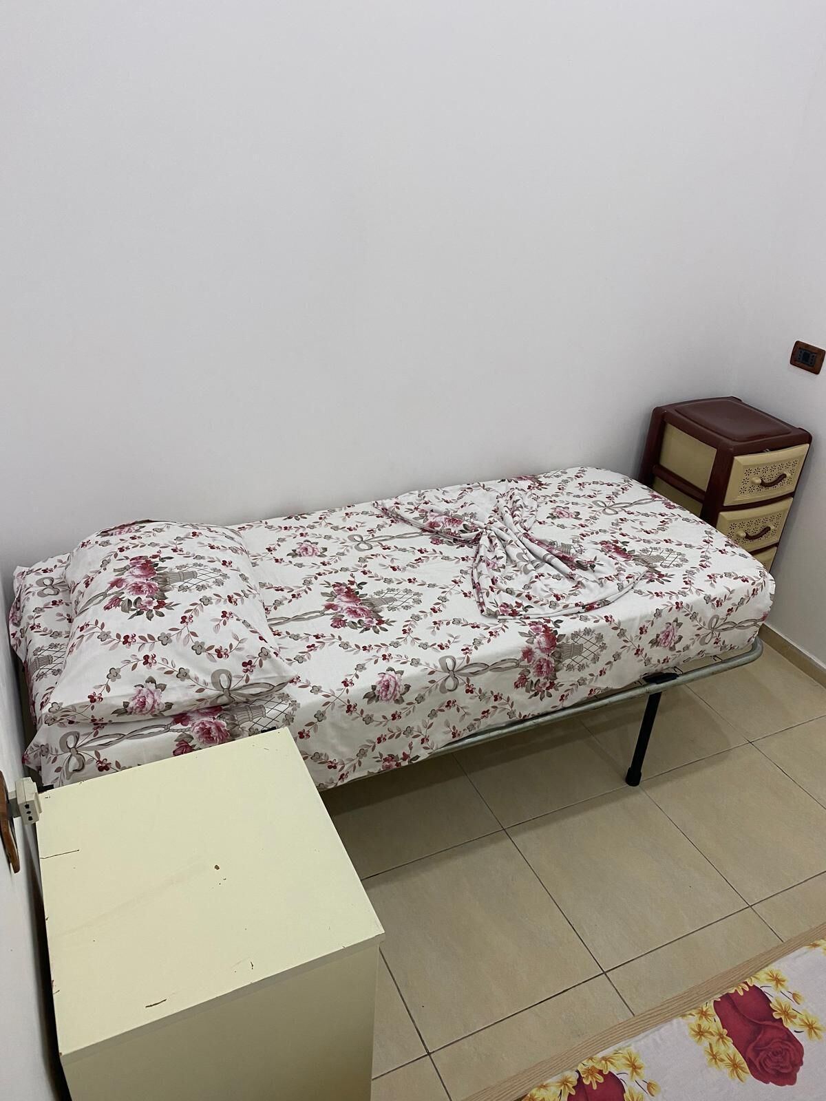 A small, single-bed room with a floral bedspread, a bedside table, and a small dresser.