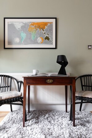 A room with a framed world map on the wall, a table with a lamp, and two chairs. - Remington Street - Four Bedroom Apartment, Sleeps 6 (London)