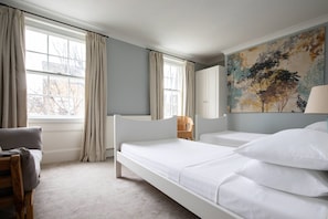 Ein Hotelzimmer mit einem Einzelbett, einem Sessel, einem Fenster mit Vorhängen und einem Gemälde an der Wand.