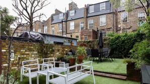 A patio with white furniture, a brick wall, and a small garden area. - Remington Street - Four Bedroom Apartment, Sleeps 6 (London)