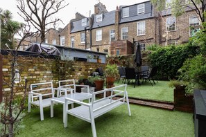 Eine Terrasse mit weißer Möbel, einer Backsteinmauer und einem kleinen Gartenbereich.