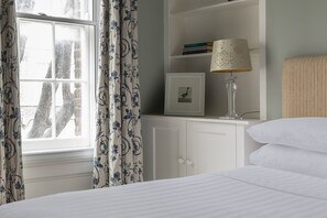 A bedroom with a bed, a bedside lamp, a window with curtains, a bookshelf with books, and a framed picture. - Remington Street - Four Bedroom Apartment, Sleeps 6 (London)