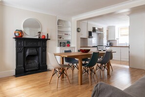 A modern kitchen with white cabinets, a wooden dining table, and a black fireplace. - Remington Street - Four Bedroom Apartment, Sleeps 6 (London)