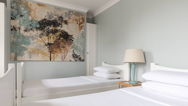 A hotel room with two single beds, a nightstand with a lamp, and a large abstract painting on the wall. - Remington Street - Four Bedroom Apartment, Sleeps 6 (London)