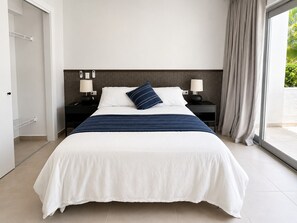 A hotel room with a large bed, two bedside tables with lamps, a view through a window, and a door leading to a closet. - Downtown PC | Pool Access | Walk to Coco Bongo (Punta Cana)