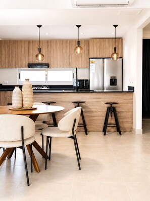 A modern kitchen with wooden cabinetry, stainless steel appliances, and pendant lighting. - Poolside condo Downtown Punta Cana &$& (Punta Cana)