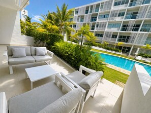 A modern hotel balcony with a pool, outdoor seating, and lush greenery. - Poolside condo Downtown Punta Cana &$& (Punta Cana)