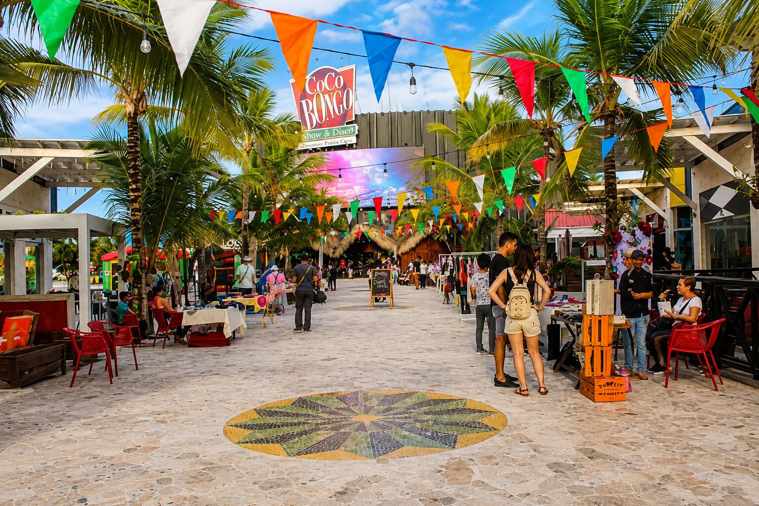 Un área de mercado al aire libre con un letrero de Coco Bongo, palmeras y un piso de baldosas con un diseño circular de mosaico.