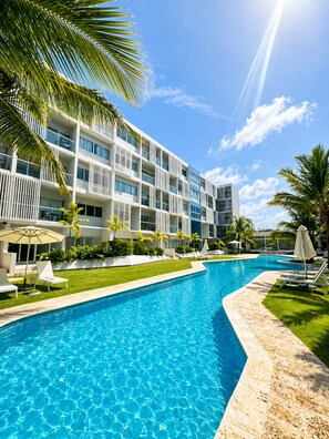 A modern hotel with a swimming pool, palm trees, and a clear blue sky. - Downtown PC | Pool Access | Walk to Coco Bongo (Punta Cana)