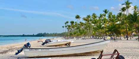 Une plage où se trouvent plusieurs bateaux, dont un blanc portant l’inscription « PAMELA MAR-1 » et un rouge portant l’inscription « TIT GUARA ».