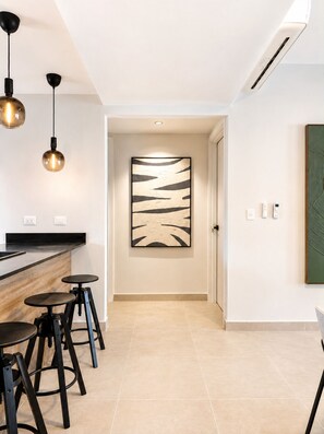 A modern kitchen with a black countertop, two black stools, pendant lighting, and a large abstract painting on the wall. - Downtown PC | Pool Access | Walk to Coco Bongo (Punta Cana)