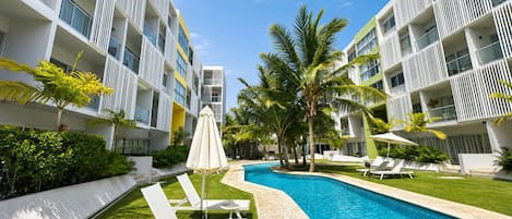 Un hôtel moderne doté d’une piscine, de chaises longues et de palmiers.