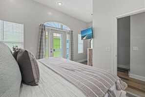 A bedroom with a bed, a television on a stand, a door leading to a balcony, and a window with blinds. - Gulf-View Retreat: Walk to Beach & Pier Park (Panama City Beach)