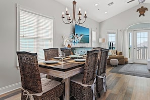 A dining area with a wooden table, wicker chairs, and a chandelier. - Gulf-View Retreat: Walk to Beach & Pier Park (Panama City Beach)