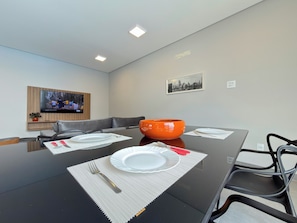 A modern dining area with a large table set for four, a television mounted on the wall, and a framed cityscape picture.